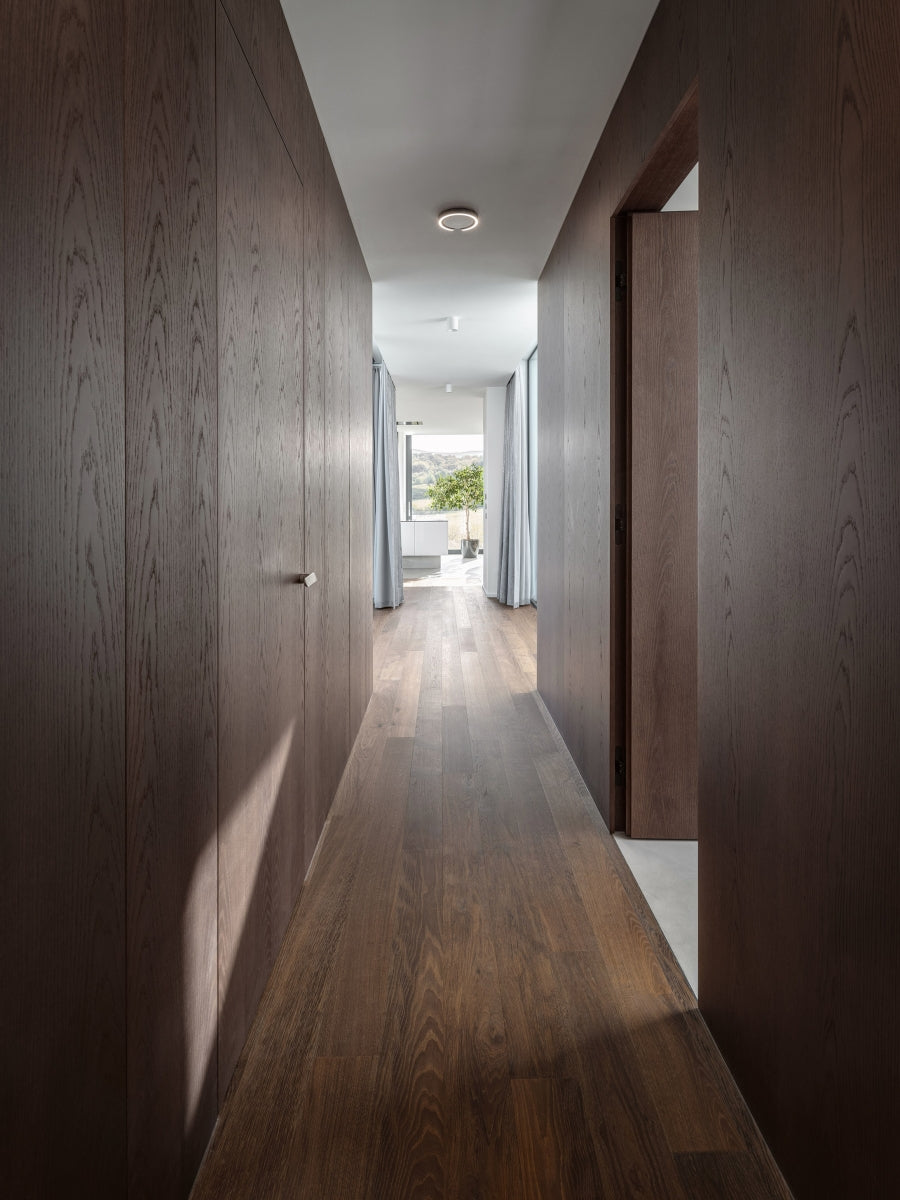 M&T Minimal 2.0 door handles in satin nickel finish featured on concealed doors in a wood veneer panel wall hallway — project "House in the Clouds" by BOQ Architekti.