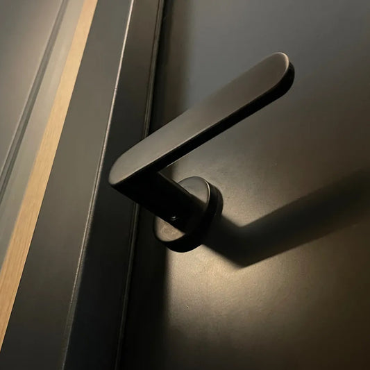 Modern black European style door lever handle (flat oval shape) on a black door. M&T Nova with a round (circle) escutcheon. Available at store.angelbau.com.